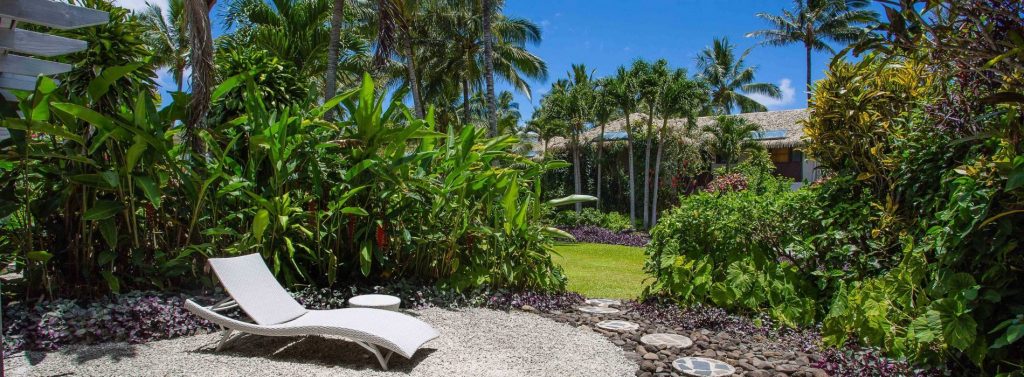 image on a sun deck lounge on a stunning private back yard surrounded by lush garden, featuring pebbles and paved-stepping-stone that leads to the open lawn